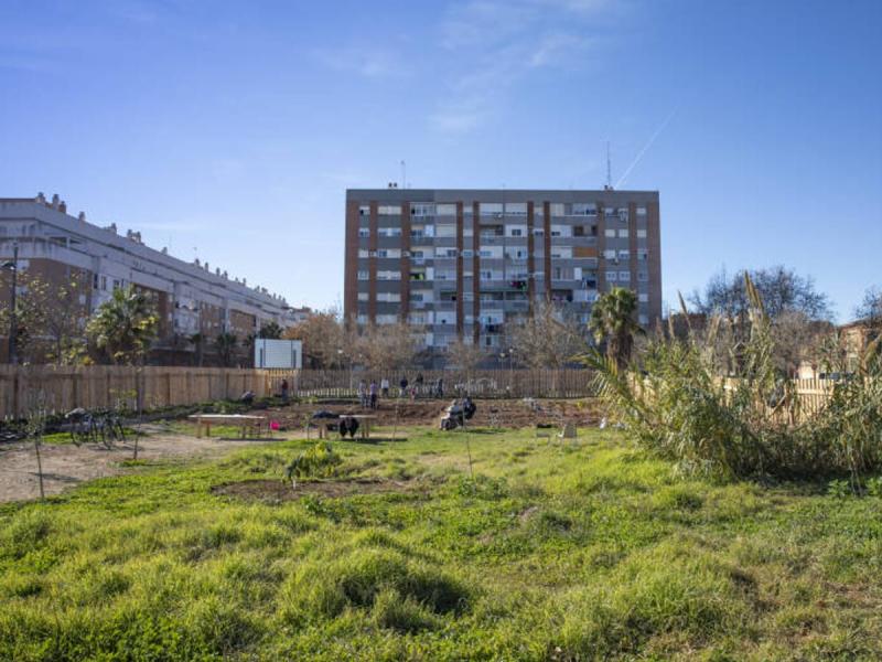 Terreno del huerto comunitario Espai Verd Benicalap en construcción, con bloques de viviendas al fondo